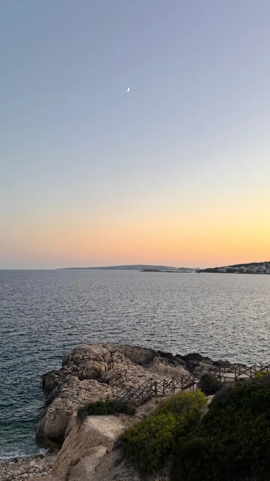 Felsküste auf Mallorca mit Holzsteg, Steinen und ruhigem Meer in der Abenddämmerung