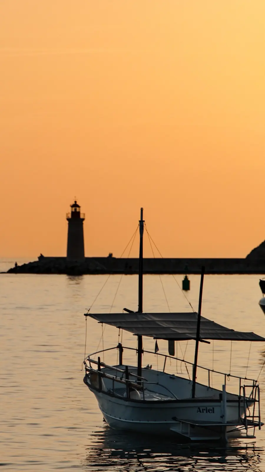 Boot 'Ariel' im Hafen vor Leuchtturm bei goldenem Sonnenuntergang auf Mallorca