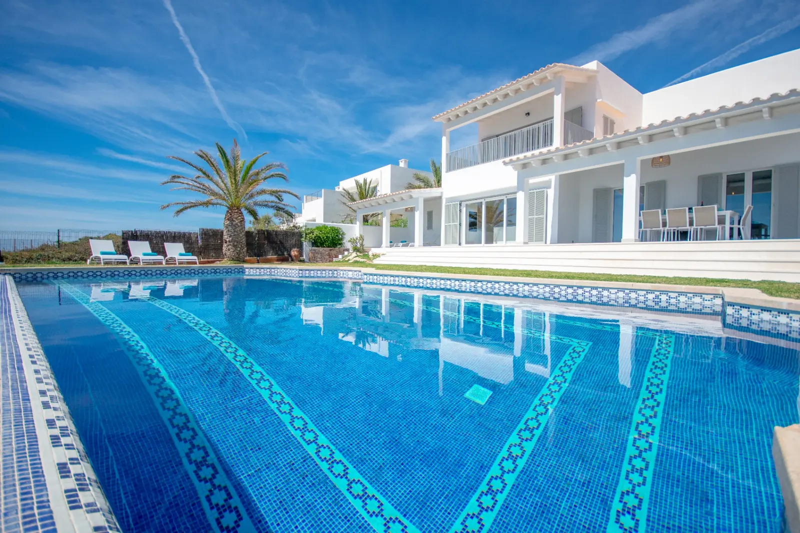 Großer Pool mit blauem Mosaik vor einer weißen Villa mit Palme auf Mallorca