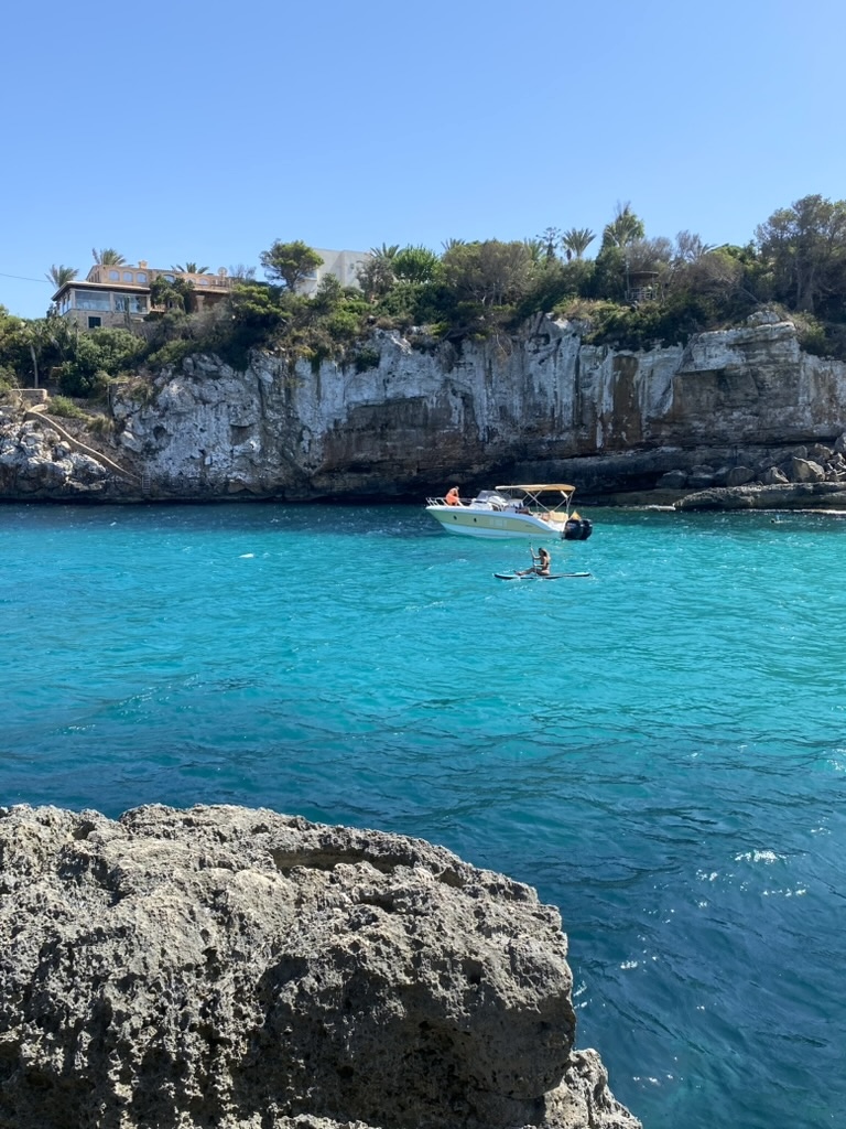 Türkise Bucht mit Boot und Stand-Up-Paddler vor Kalkfelsen