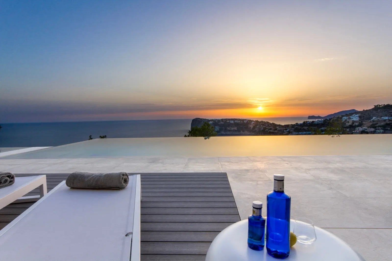 Sonnenuntergang über dem Meer mit Infinity-Pool und Sonnenliegen im Vordergrund