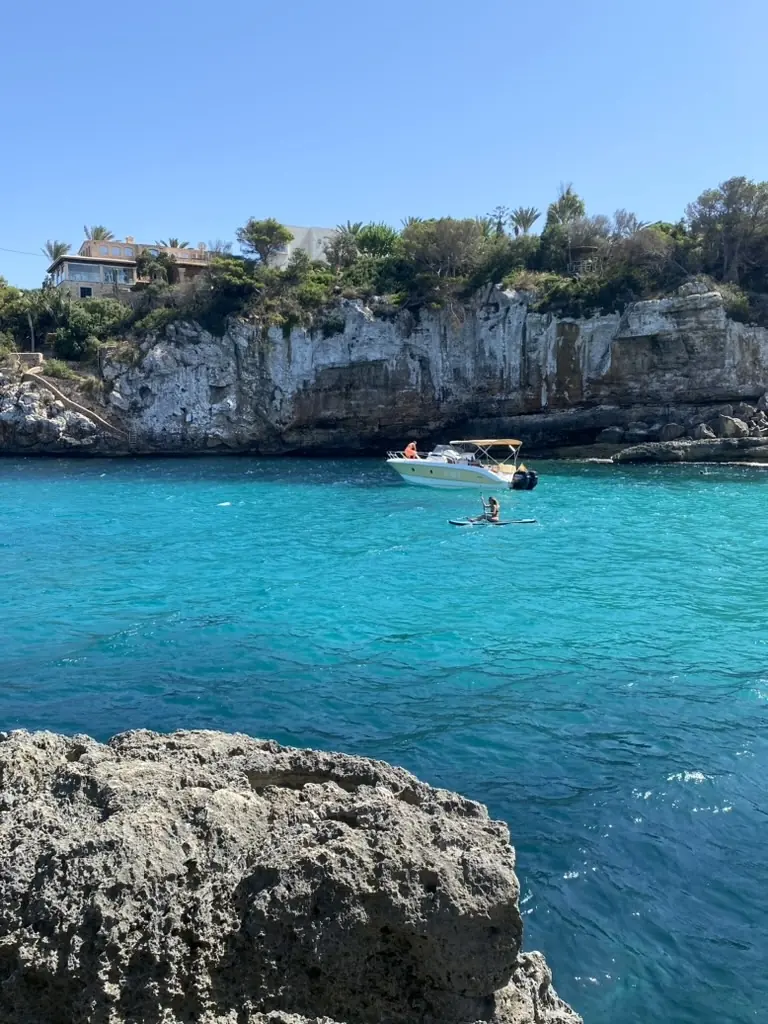 Türkisblaue Bucht auf Mallorca mit Felsen, Motorboot und Villa auf dem Kliff