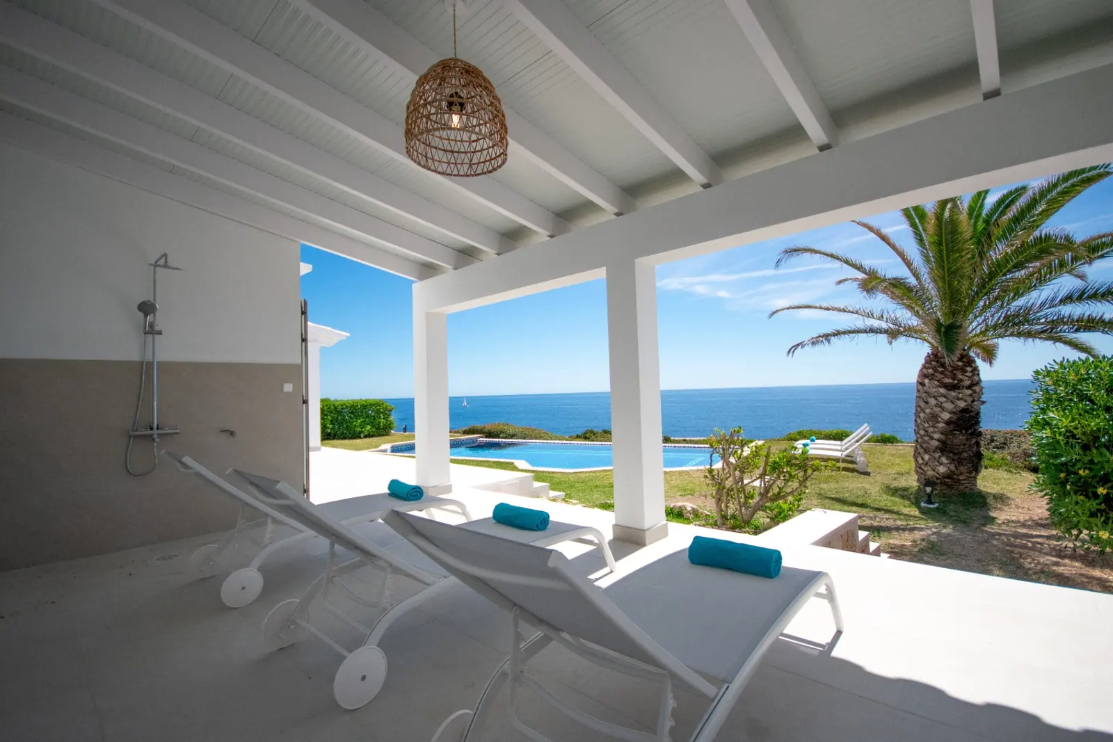 Sonnenliegen unter Pergola mit Outdoor-Dusche und Blick auf den Pool und das Meer